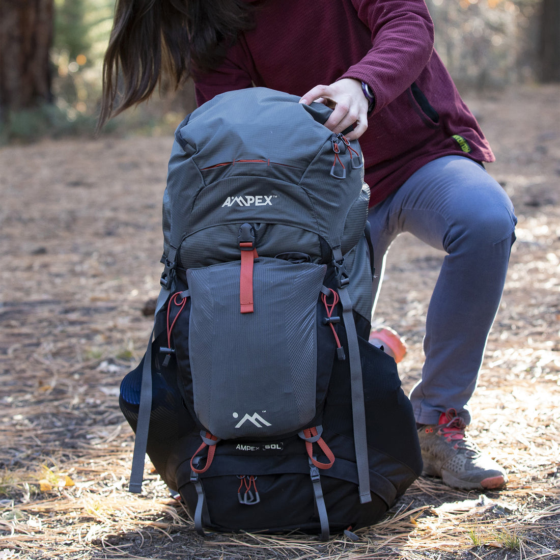 Ampex hiking backpack standing upright on the ground, with a person kneeling beside it in outdoor gear.