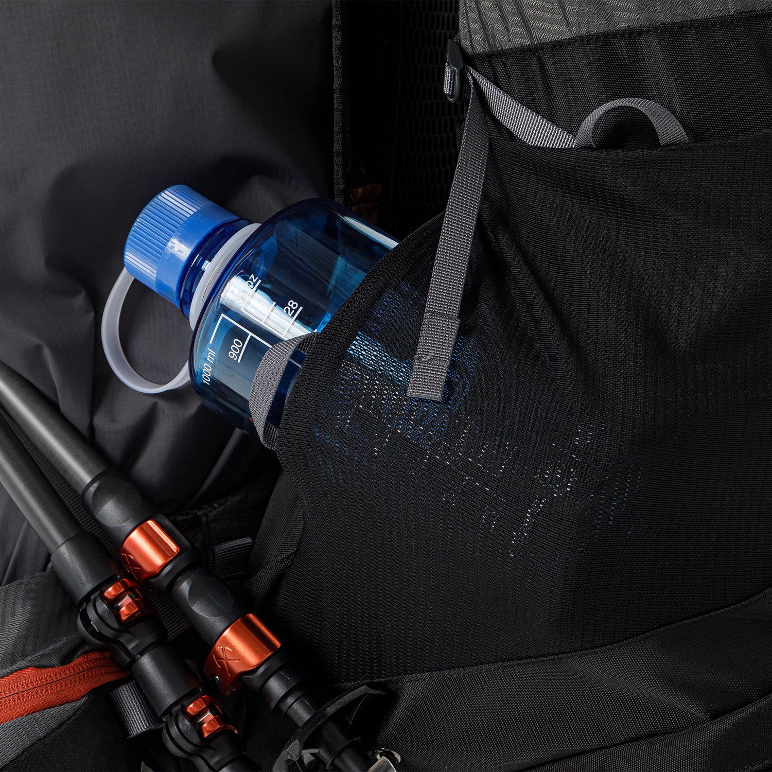 Elastic mesh side pocket carrying a slimmer water bottle with trekking poles strapped nearby.