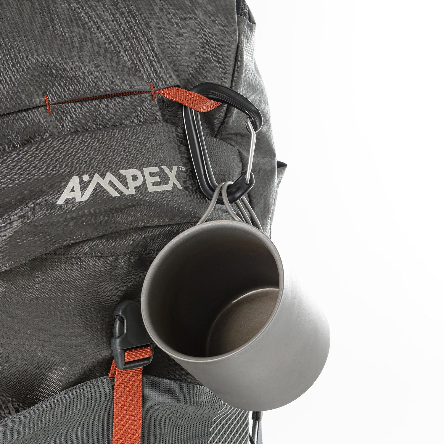 Backpack front view with a metal cup clipped to an external loop near the Ampex logo.
