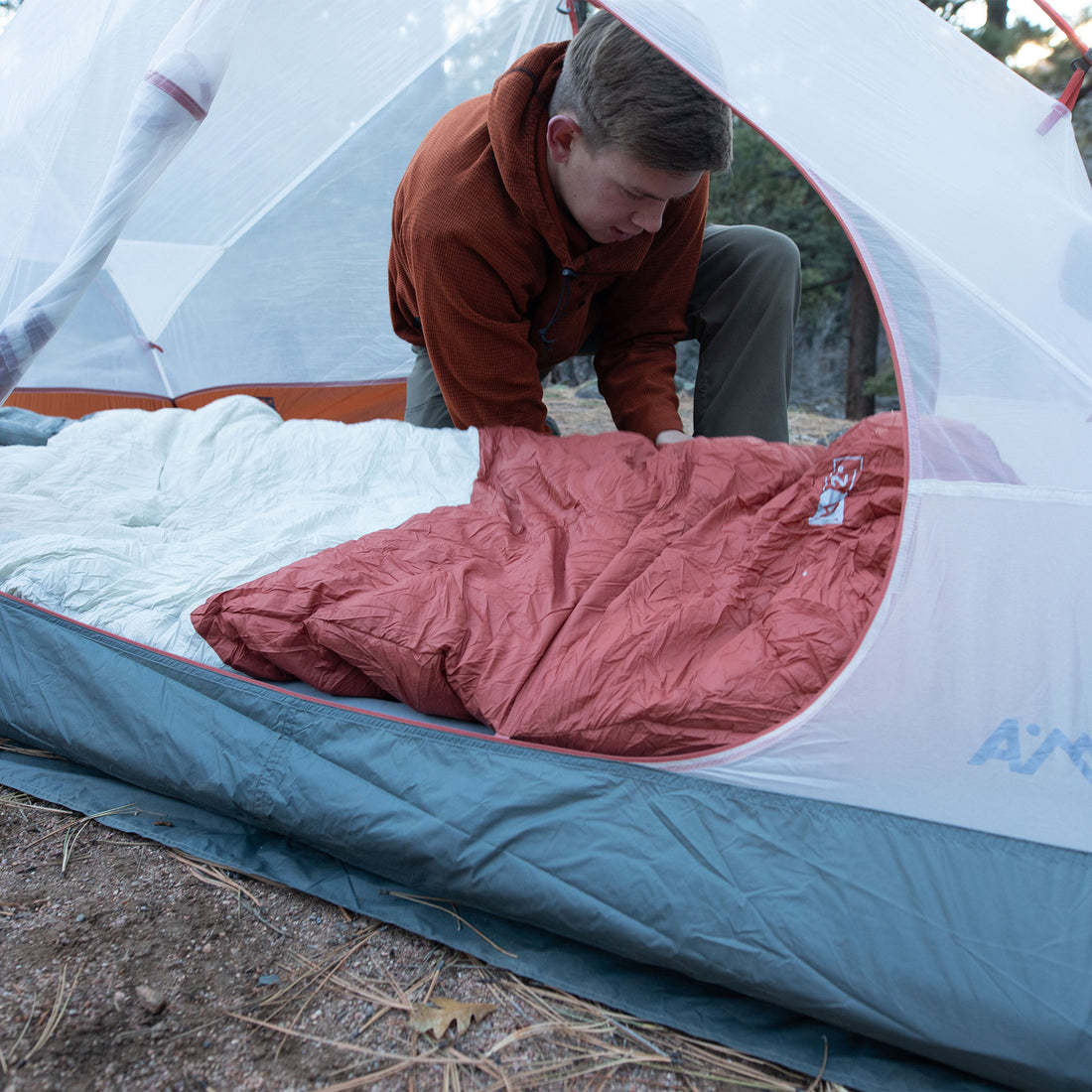 Camper laying out the sleeping bag inside a tent pitched on rocky ground.