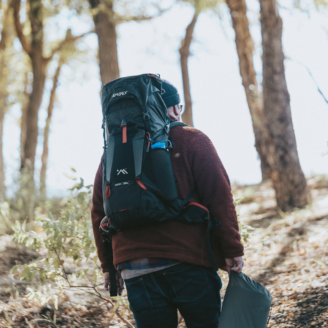 Person wearing the Ampex backpack while hiking on a forest trail.