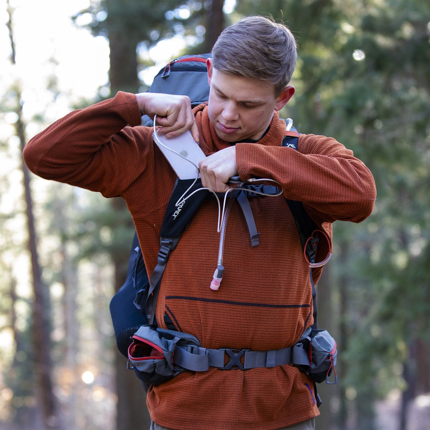 Hiker in a forest tightening the hip belt strap of the backpack for fit and support.