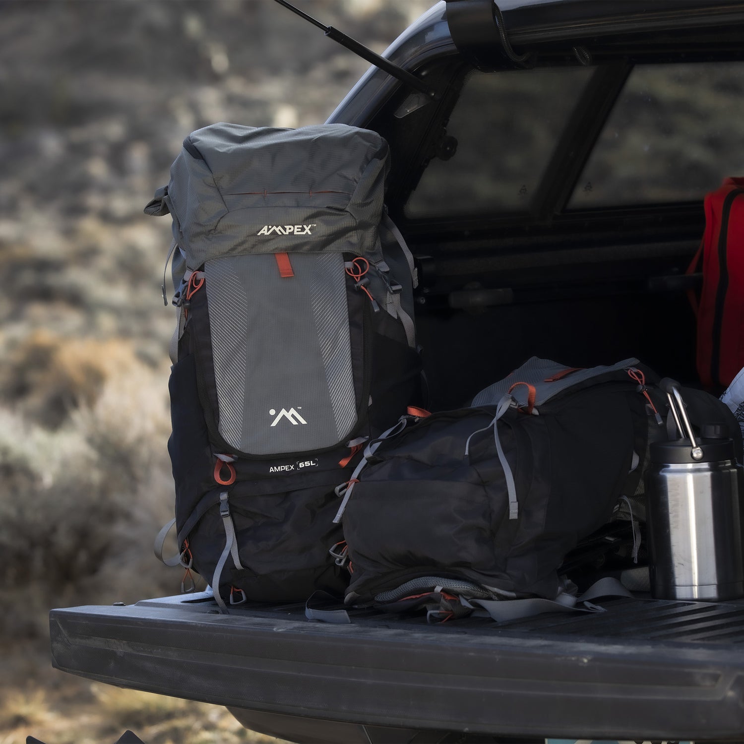 Backpack sitting on a truck tailgate beside other gear bags and camping equipment.
