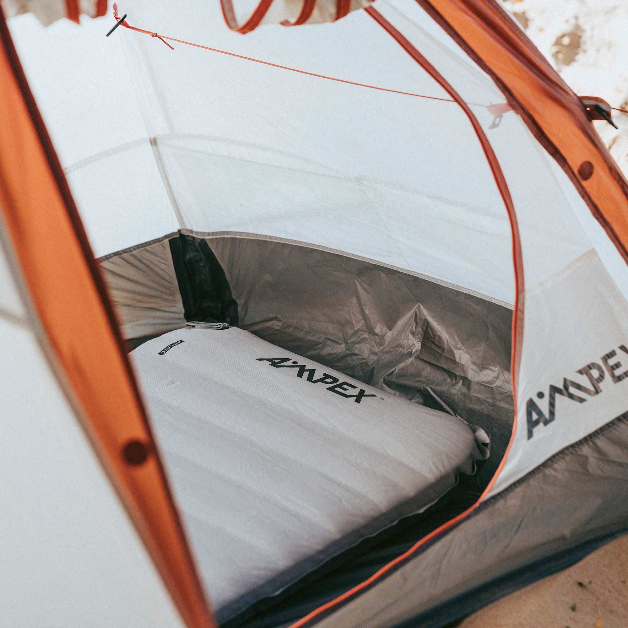 Sleeping pad placed inside a tent, partially covered by the tent flap, showing fit and thickness.