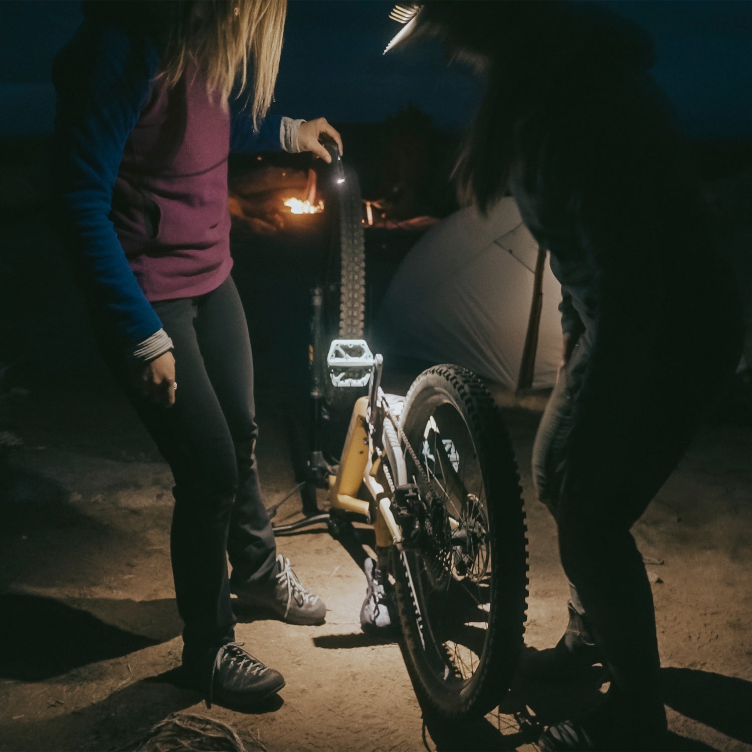 Two people using the 300 lumen light at night while fixing a mountain bike.