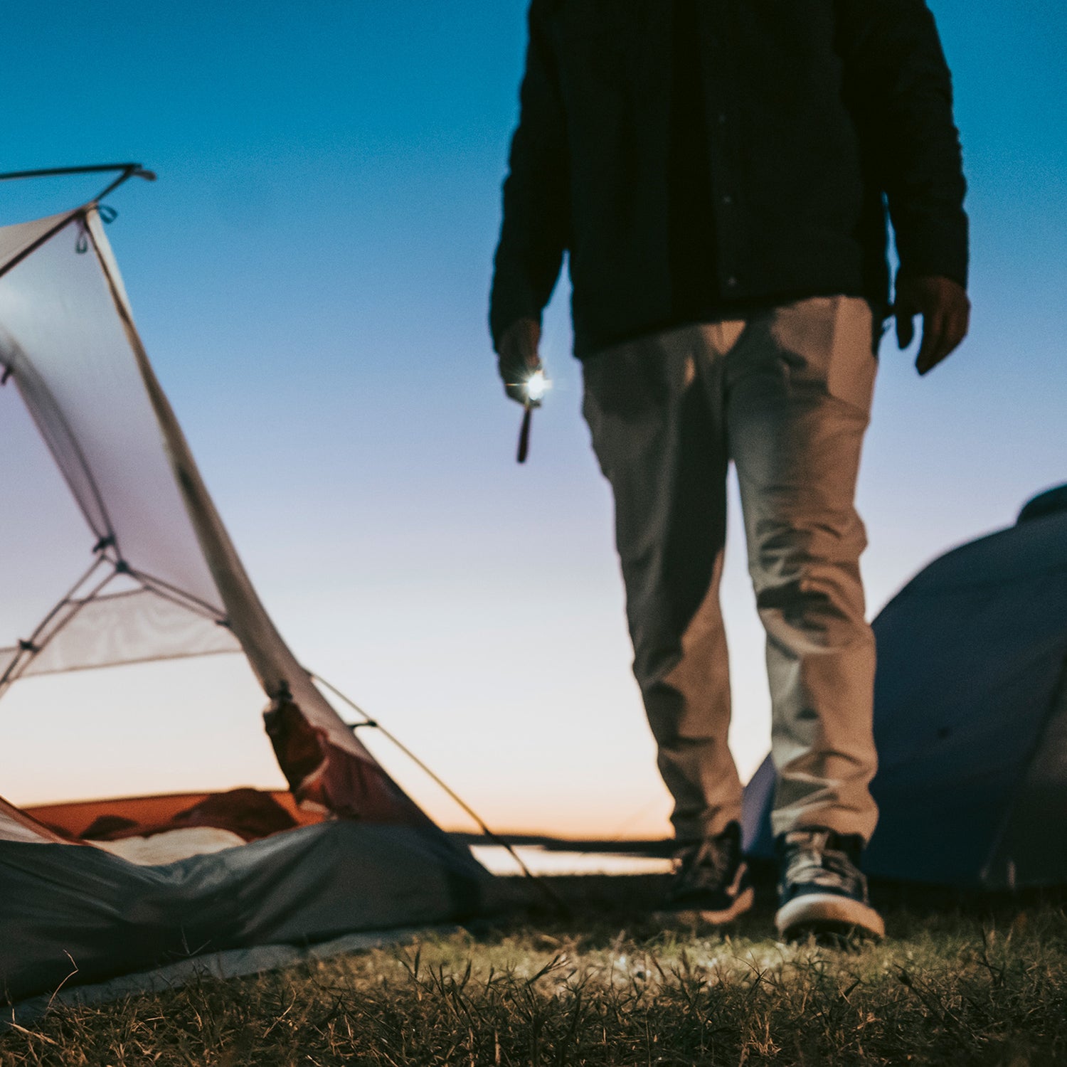 A person using the 300 lumen flashlight in the morning near a tent.