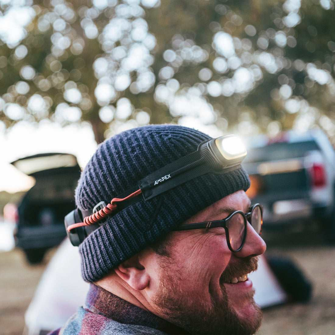A person outdoors at dusk wearing the headlamp on a beanie, smiling and facing sideways.