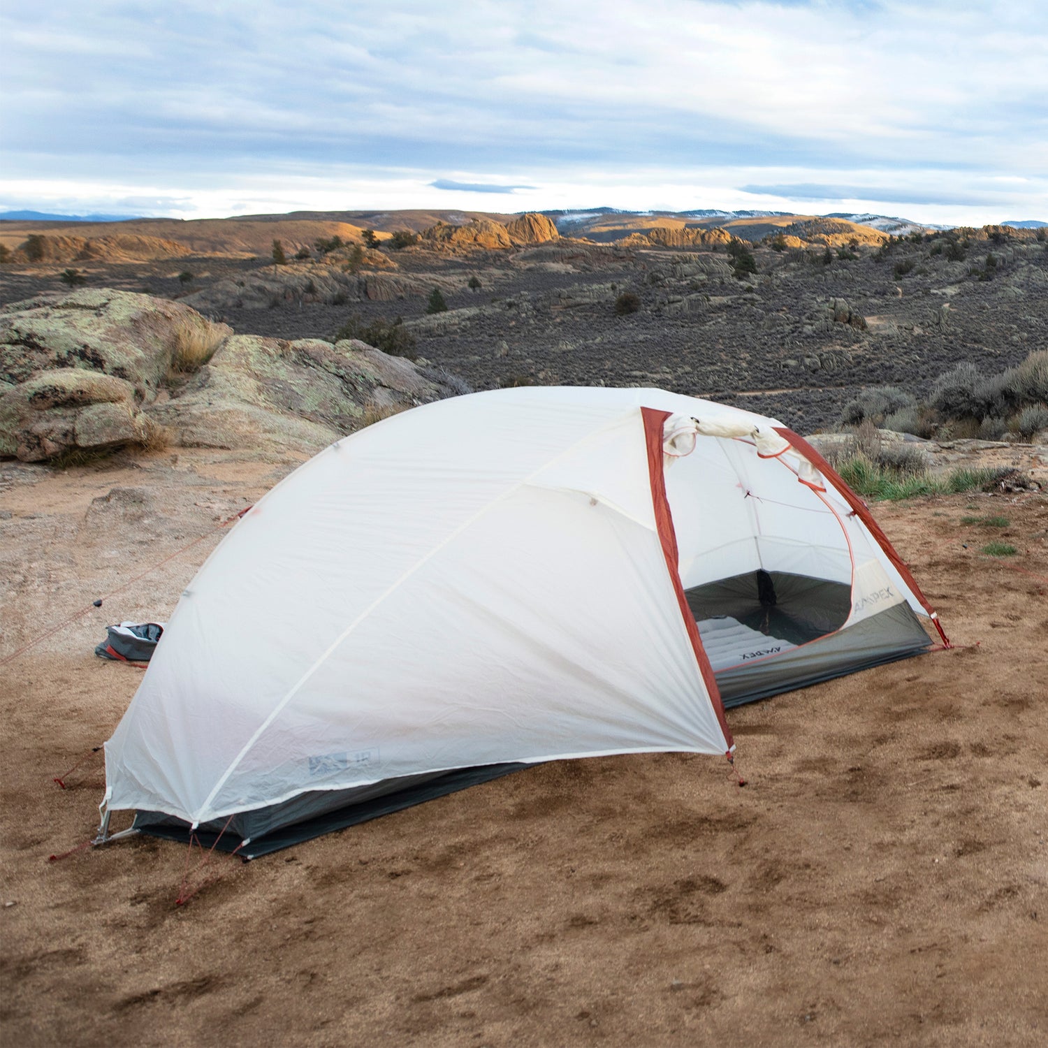 Tent pitched on dry ground in a desert landscape with mountains in background.