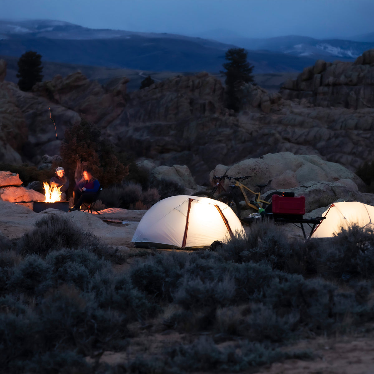 Multiple tents set up in a campsite at night with a campfire glowing nearby.