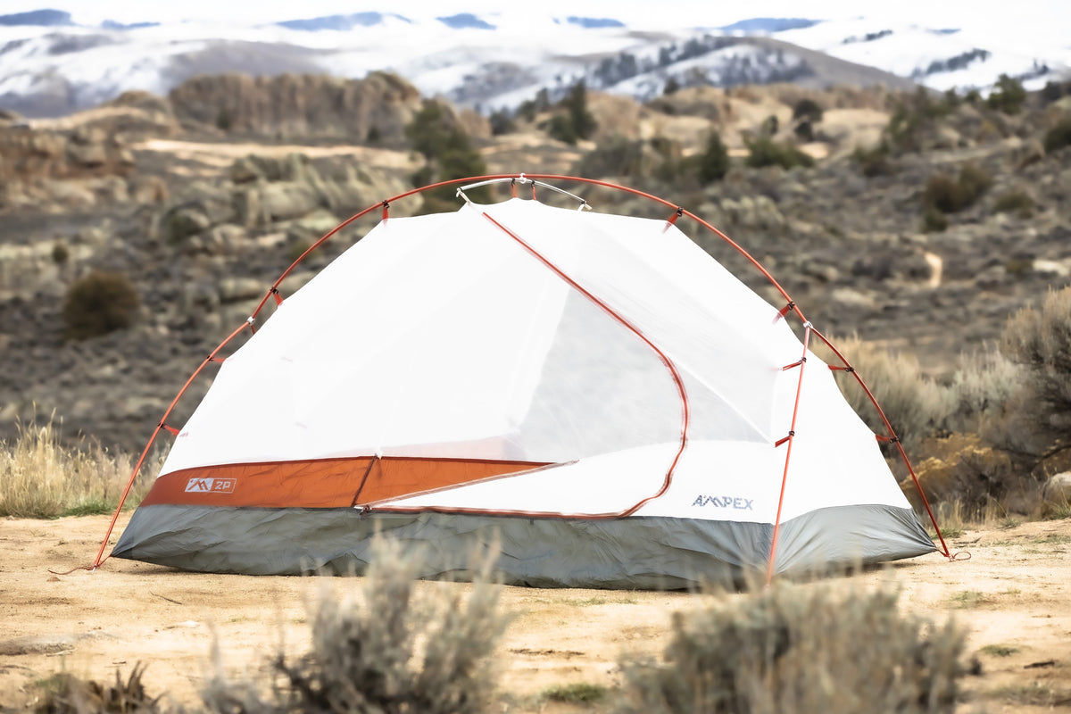 Tent pitched on dry ground in a desert landscape with mountains in background.