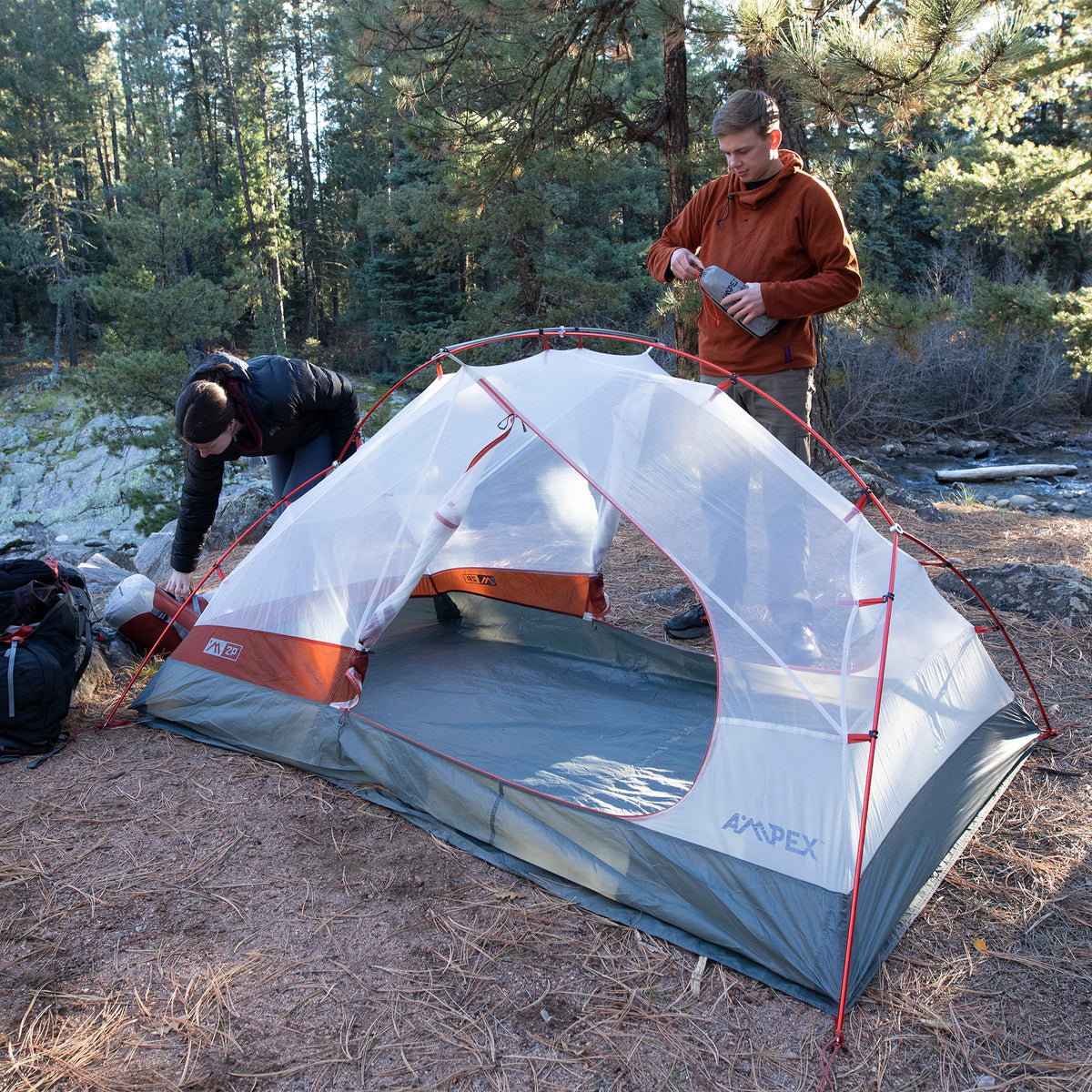 Two campers pitching the tent outdoors in a forested area.