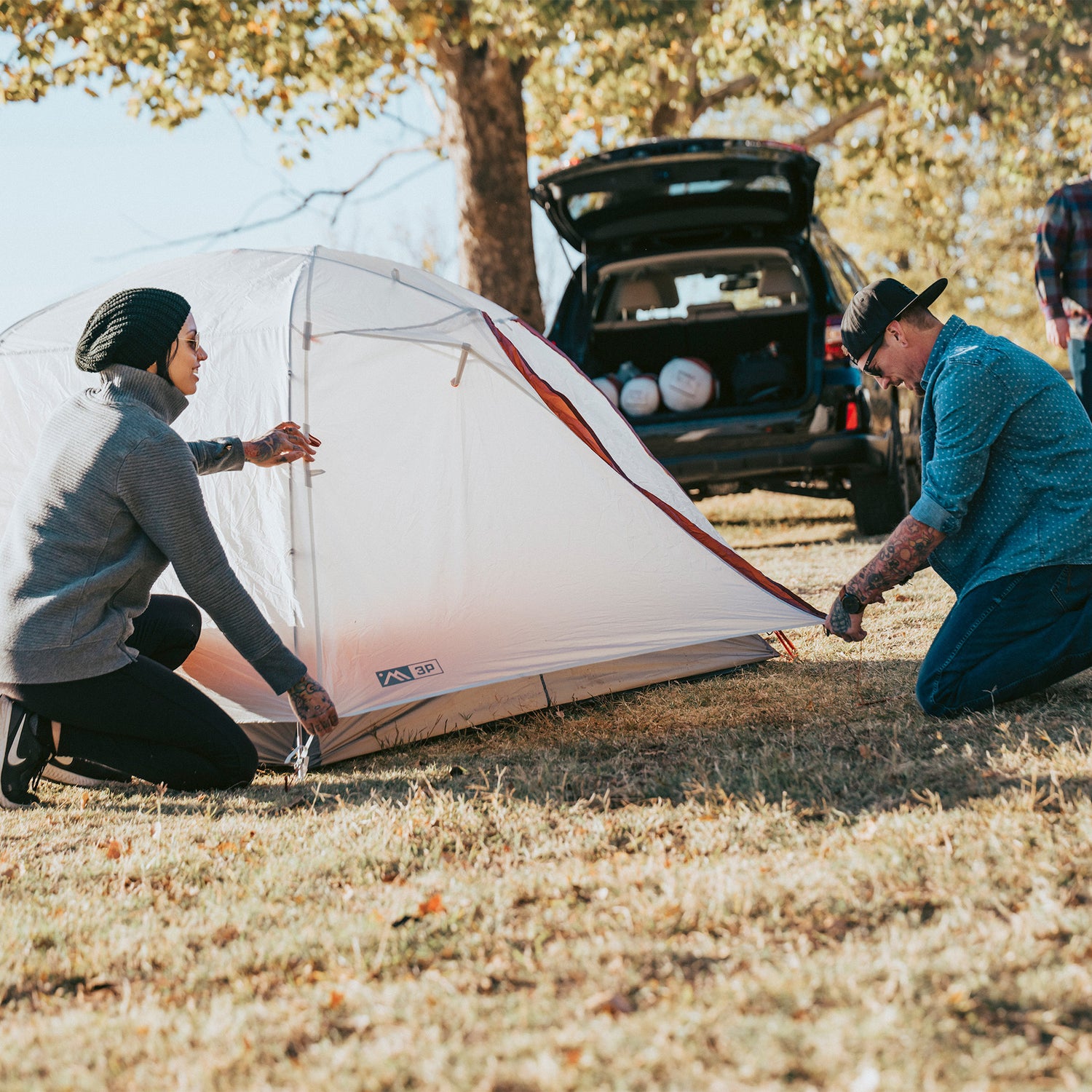 Two campers setting up the Ampex tent outdoors next to a vehicle.