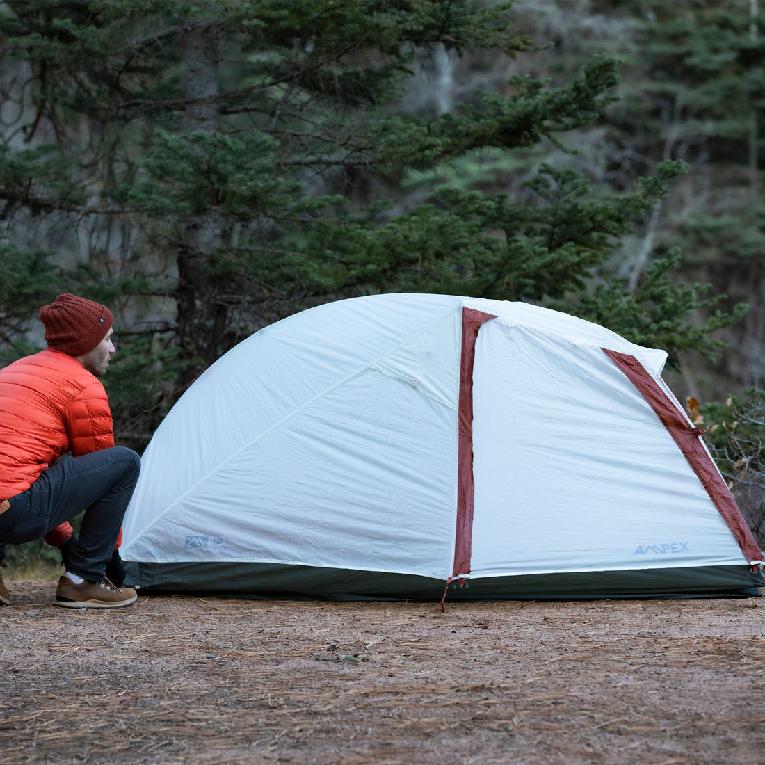 A camper pitching the tent outdoors in a forested area.